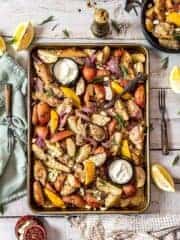 Overhead shot of on pan Mediterranean herb chicken & potato dinner served with yogurt and lemon wedges.