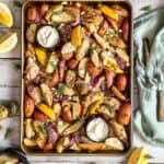 A baking tray with potato wedges, chicken breast strips, and onion with Mediterranean spices.