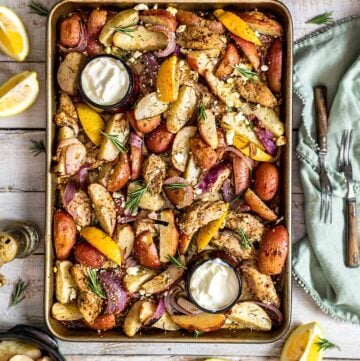 A baking tray with potato wedges, chicken breast strips, and onion with Mediterranean spices.