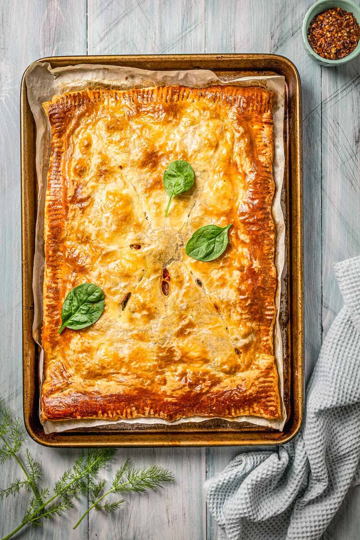 Baked slab pie in a sheet pan/cookie sheet with basil on top. 