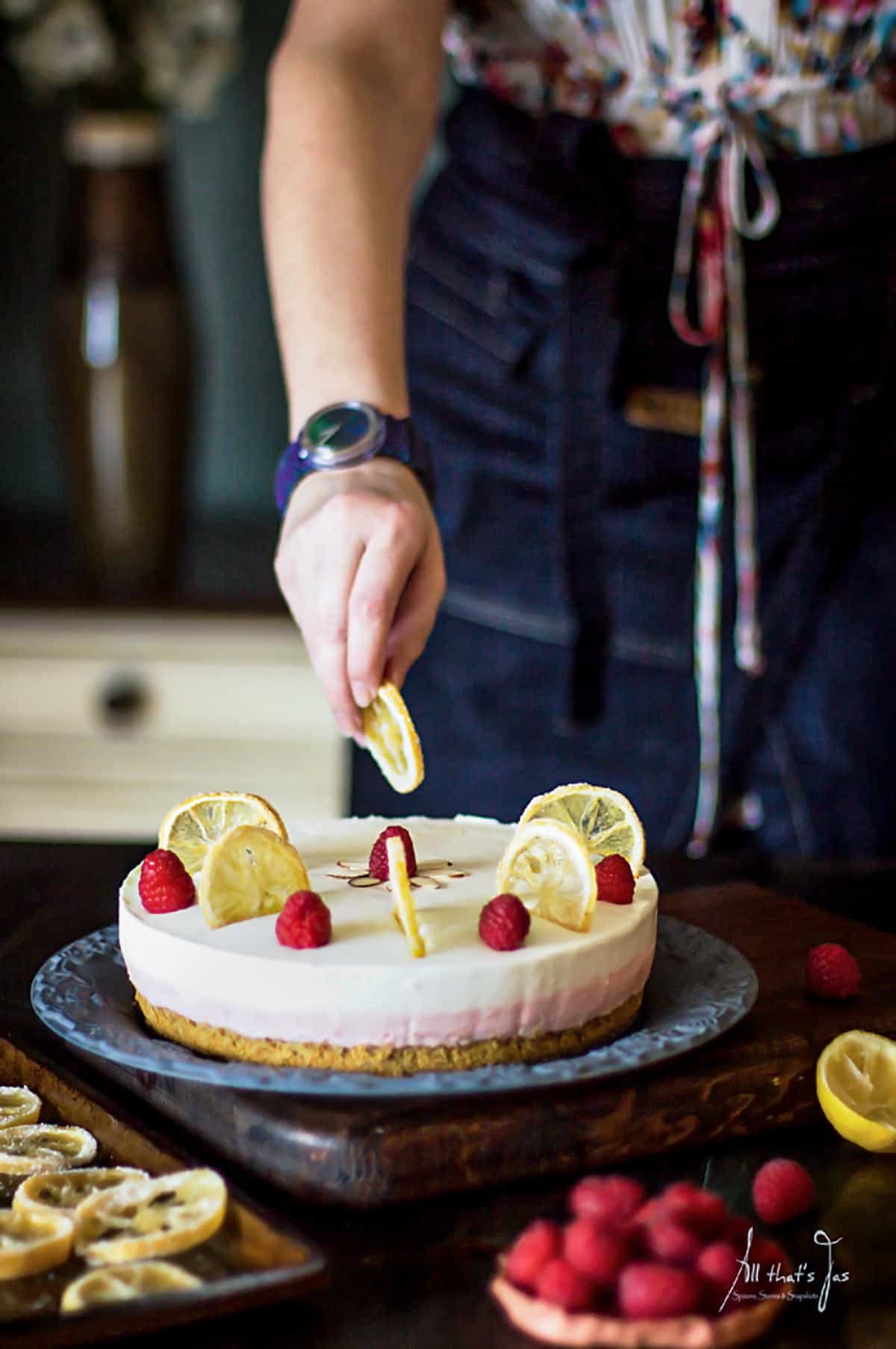 A woman placing lemon slice on a cheesecake.