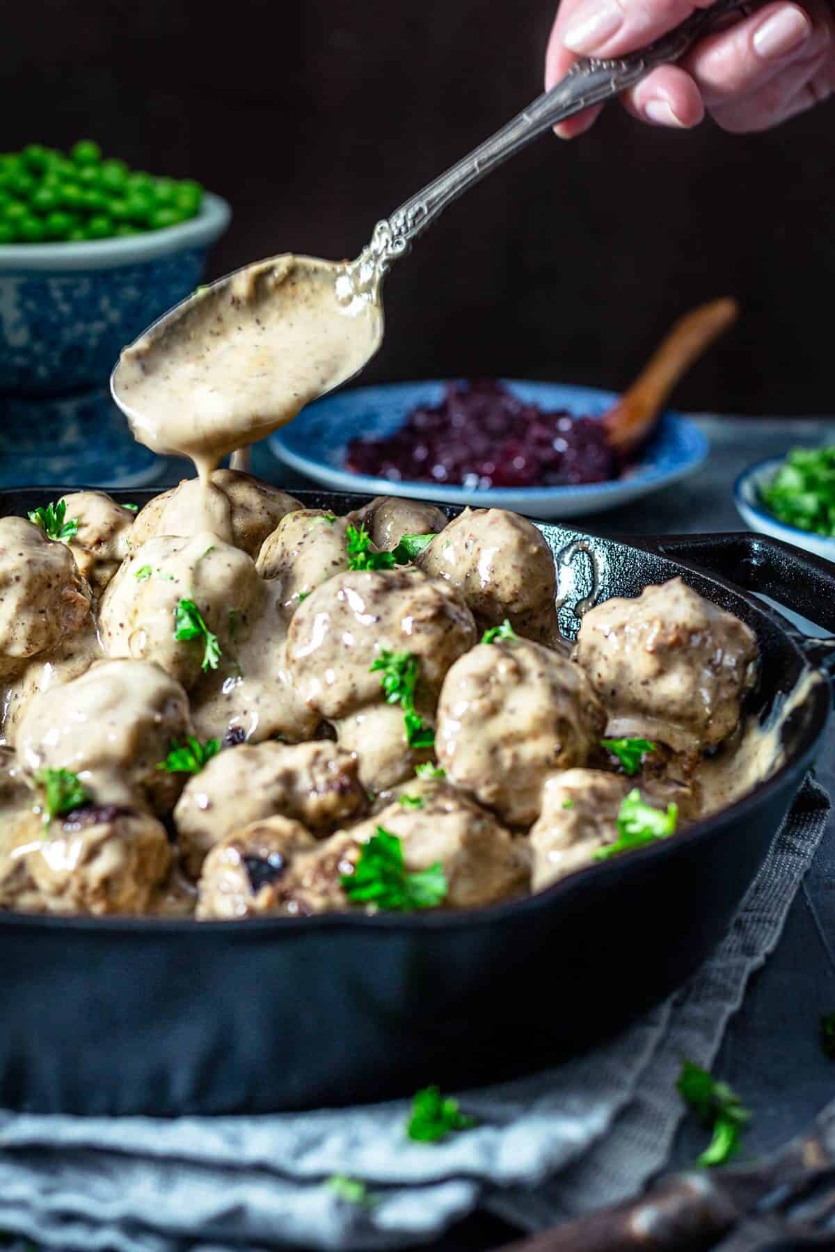 A person spooning gravy over the meatballs.