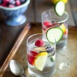 Two glasses of water with fruit inside it on a table.