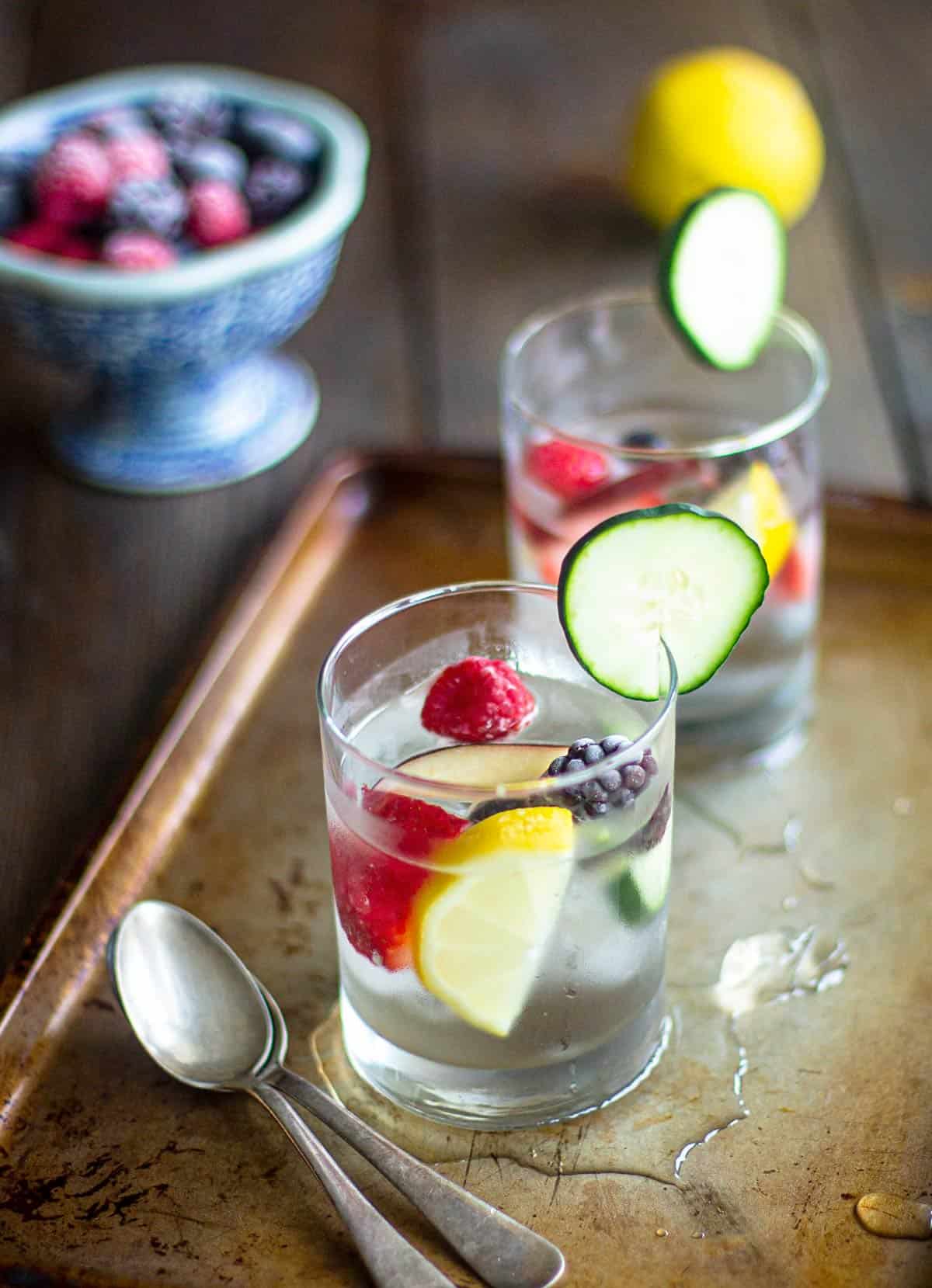 Two glasses of water with fruit inside it on a table.