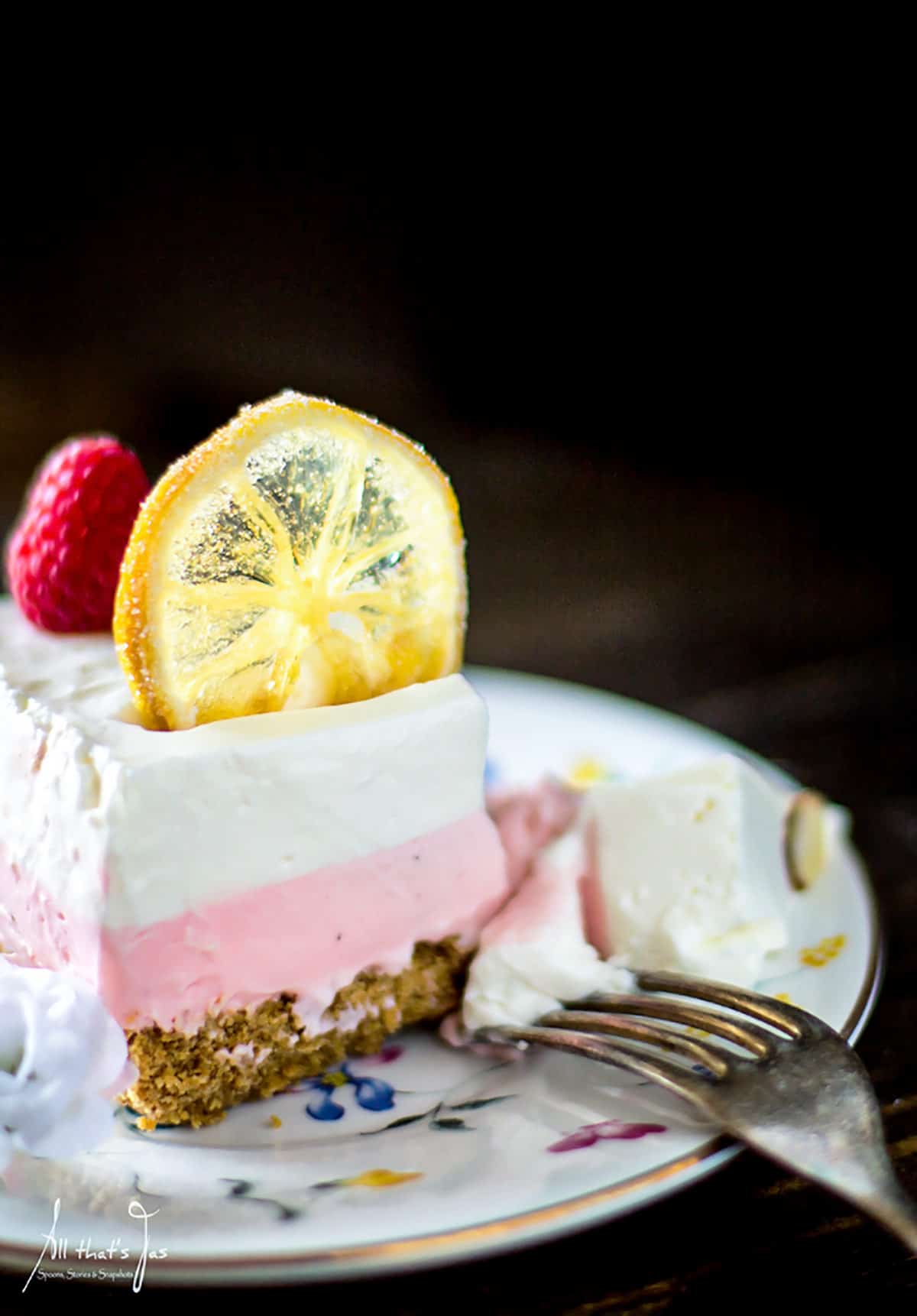 A slice of lemon raspberry cheesecake with candied lemon slice on top.