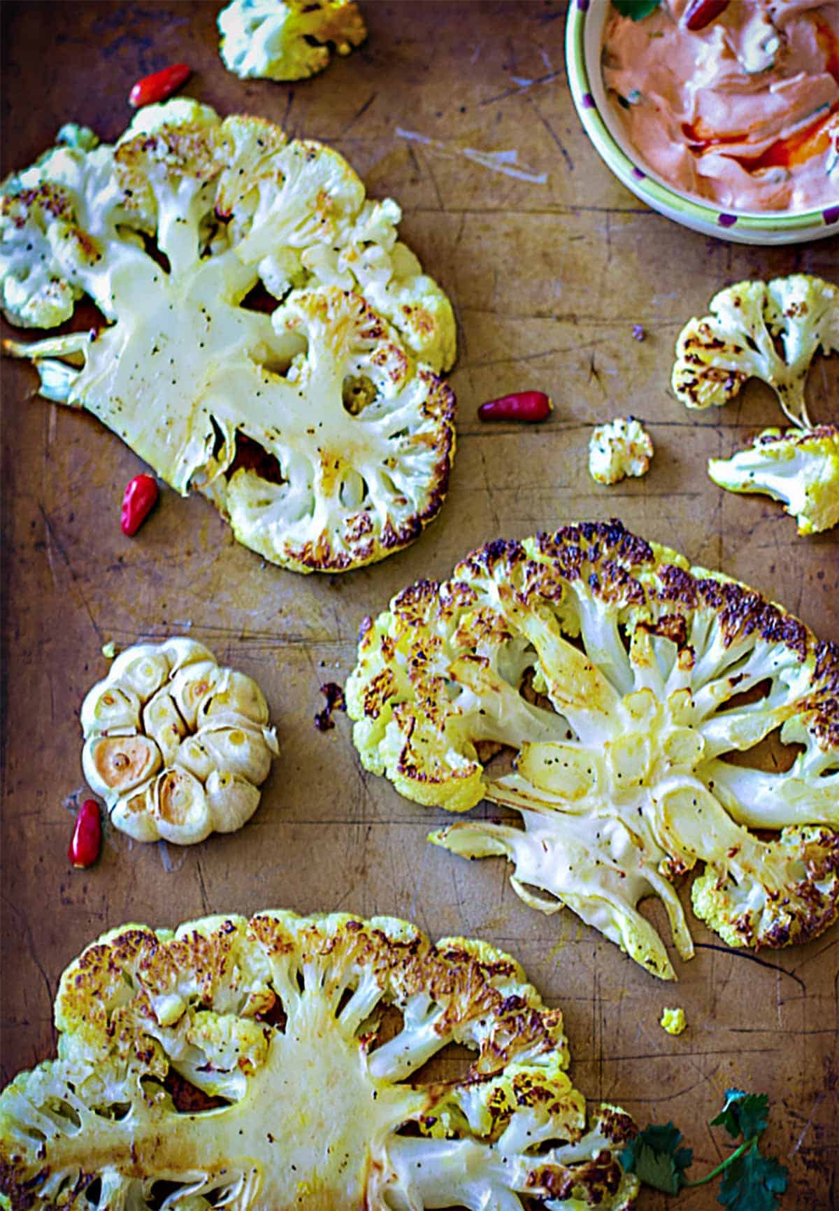 Roasted cauliflower steaks with garlic on a baking sheet.