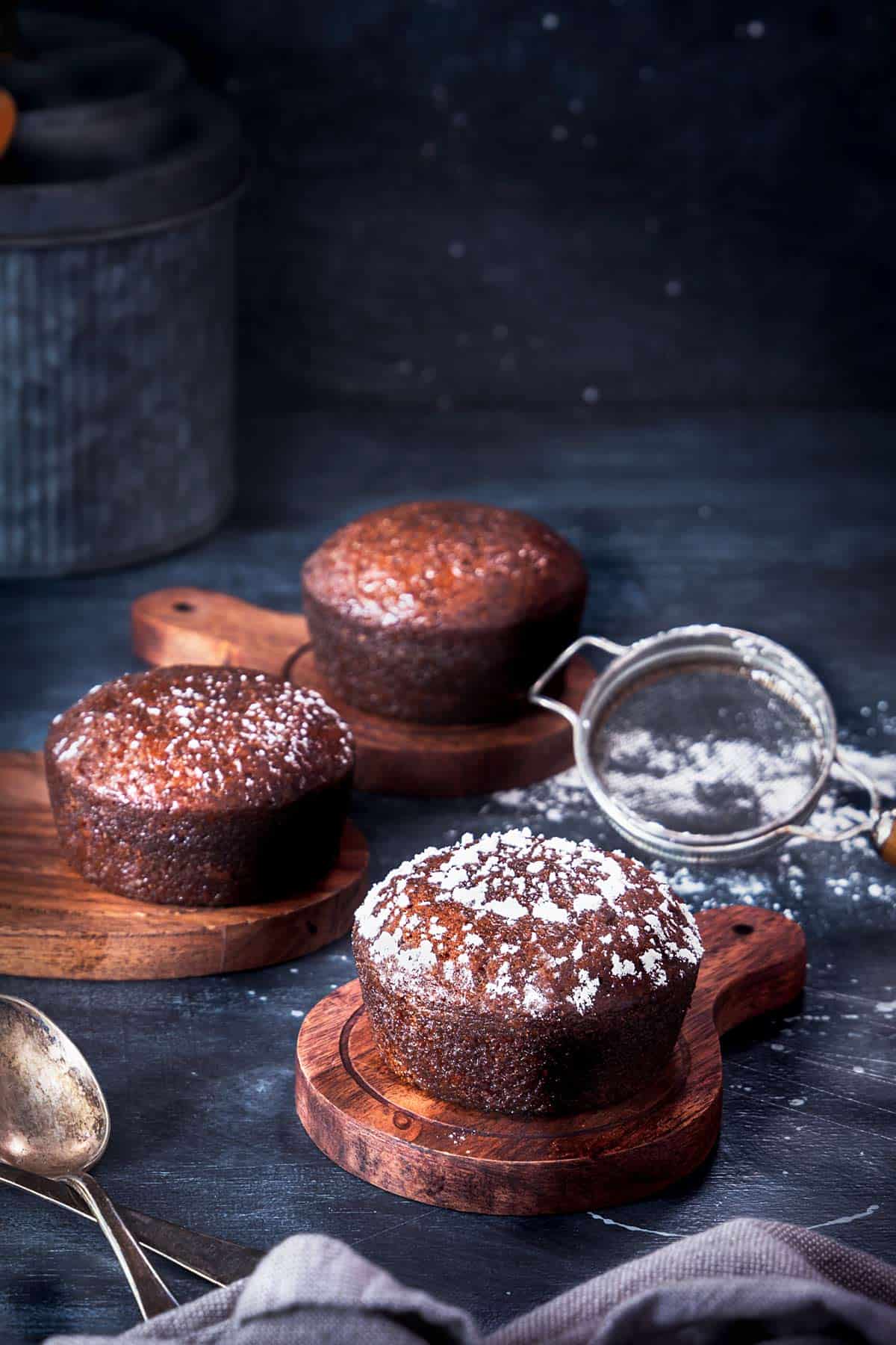 Malva pudding cakes lined up on a table topped with powdered sugar design. 