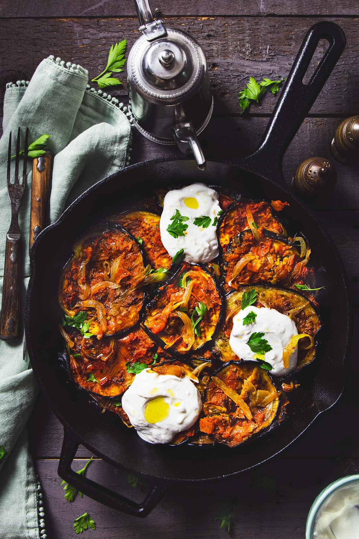 Afghan roasted eggplant in a cast iron skillet with dollops of garlic yogurt sauce.