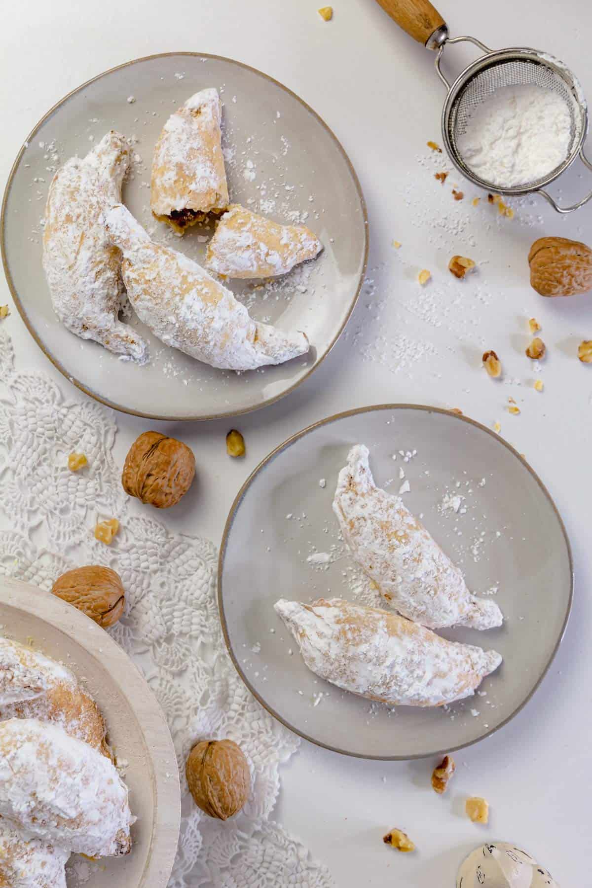 Two plates with Polish kiflies, walnuts, and powdered sugar on the table.