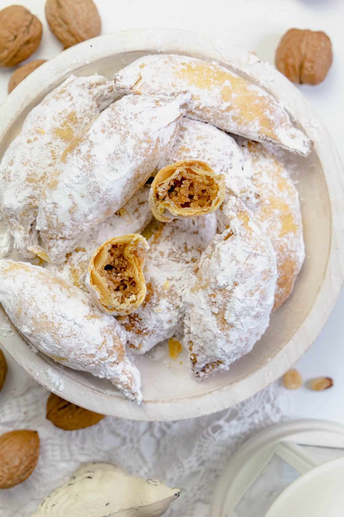 Sugar-coated kifli on a serving plate with one broken in half to show the filling.