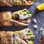 Three turkey gyros wrapped in brown paper on a table.