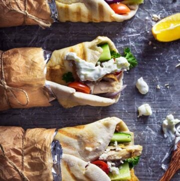 Three turkey gyros wrapped in brown paper on a table.