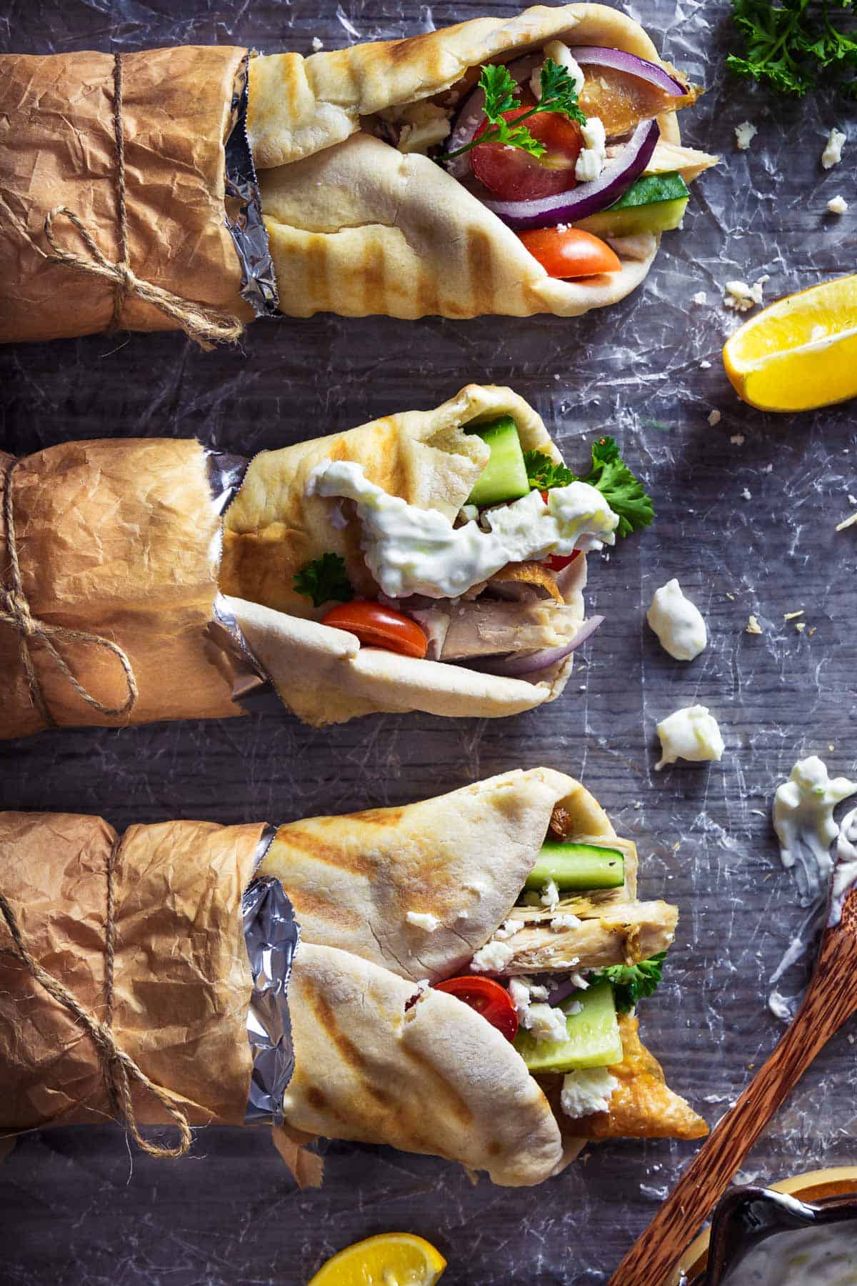 Three turkey gyros wrapped in brown paper on a table.