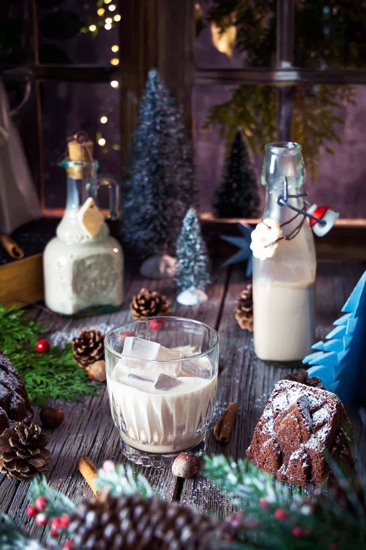 Homemade Christmas Baileys in pretty bottles and a glass on a festive-decorated table.