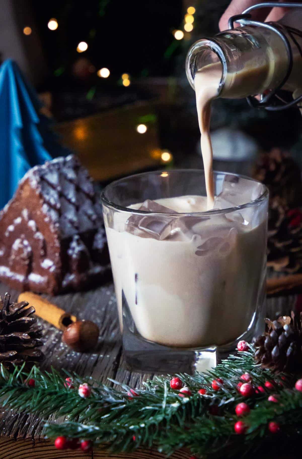 Pouring homemade Baileys into a glass over ice cubes.