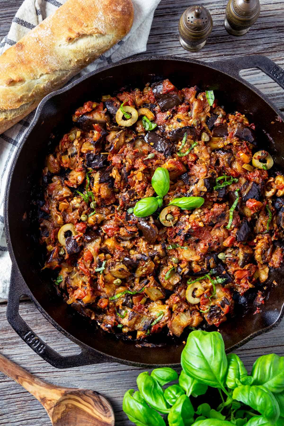Eggplant caponata dish in a cast iron skillet served with bread.