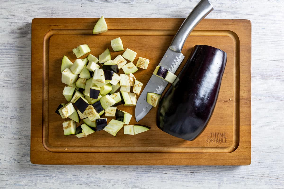 Half and diced eggplant on a cutting board with a knife.