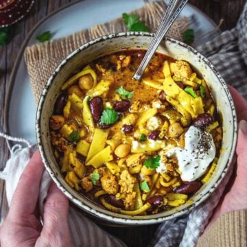 A person holding a bowl of aush - Persian chicken noodle soup.