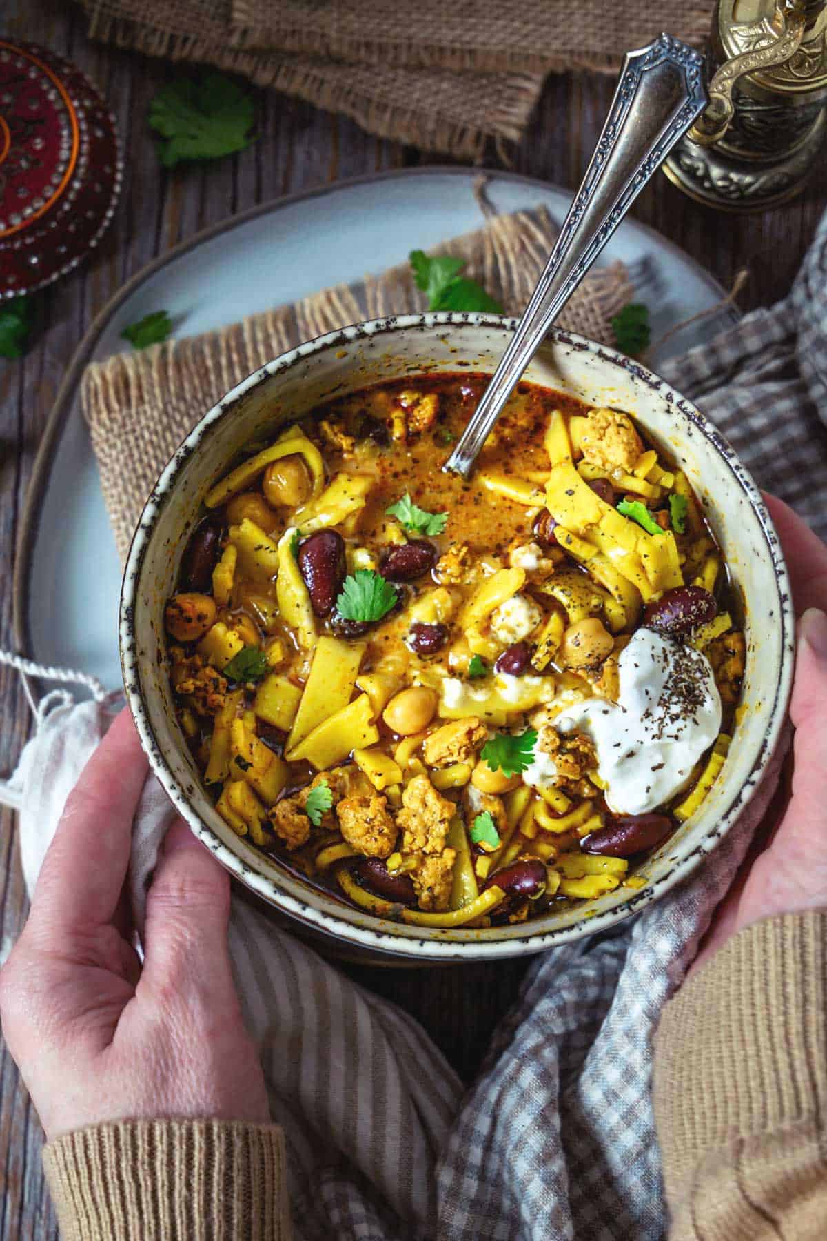 A person holding a bowl of aush -  Persian chicken noodle soup. 