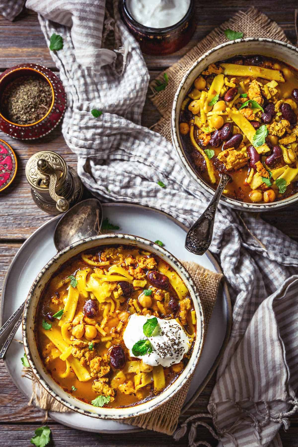 Two bowls of Afghan chicken noodle soup on a wooden table.