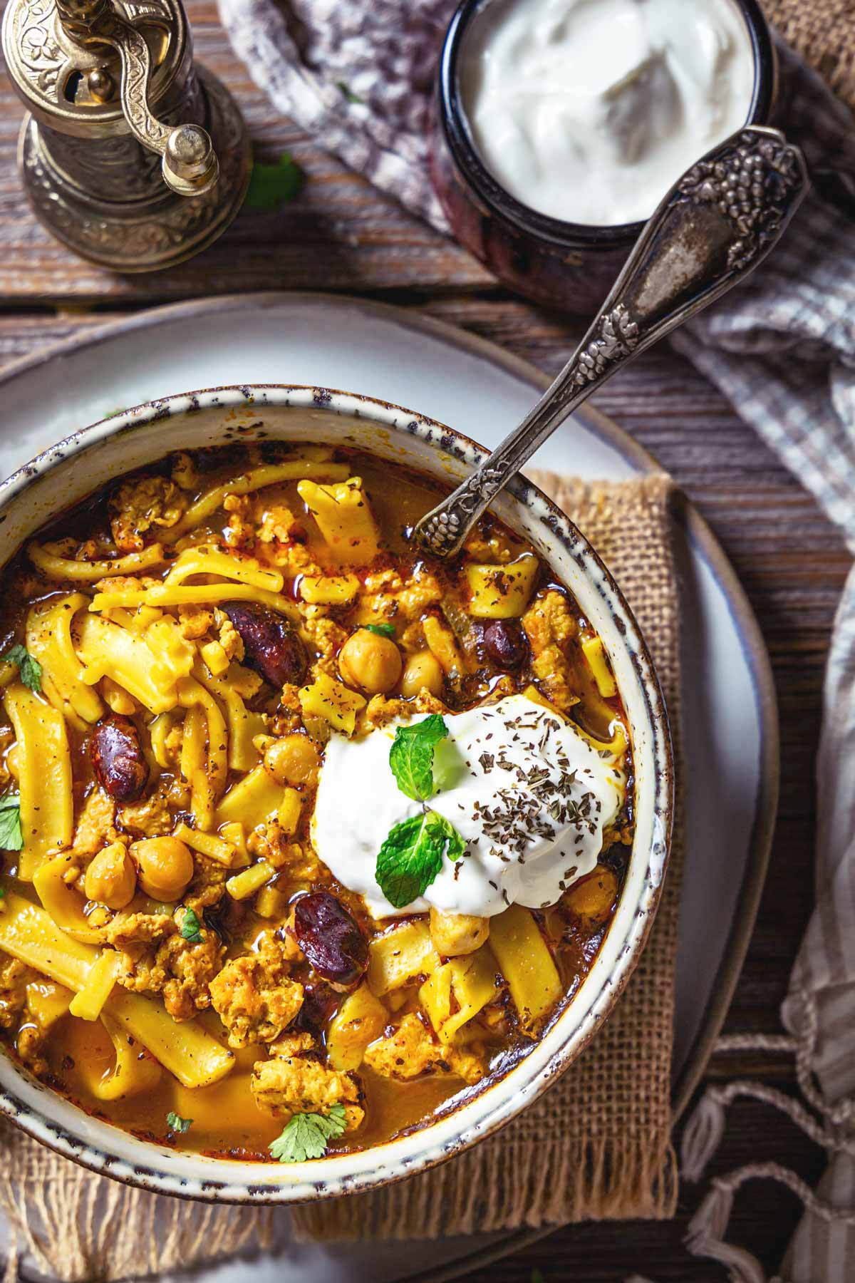 A serving of chicken noodle soup in a bowl with a dollop of yogurt on top.