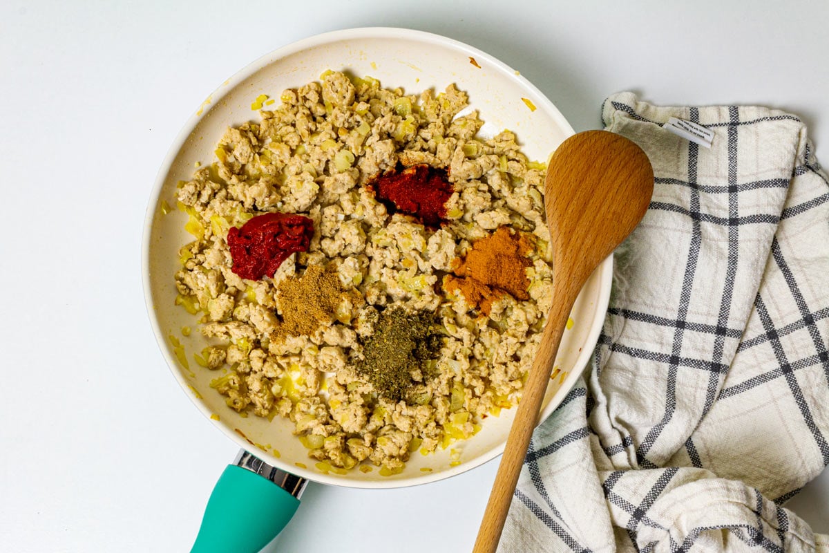 Spices over cooked ground chicken in a skillet. 