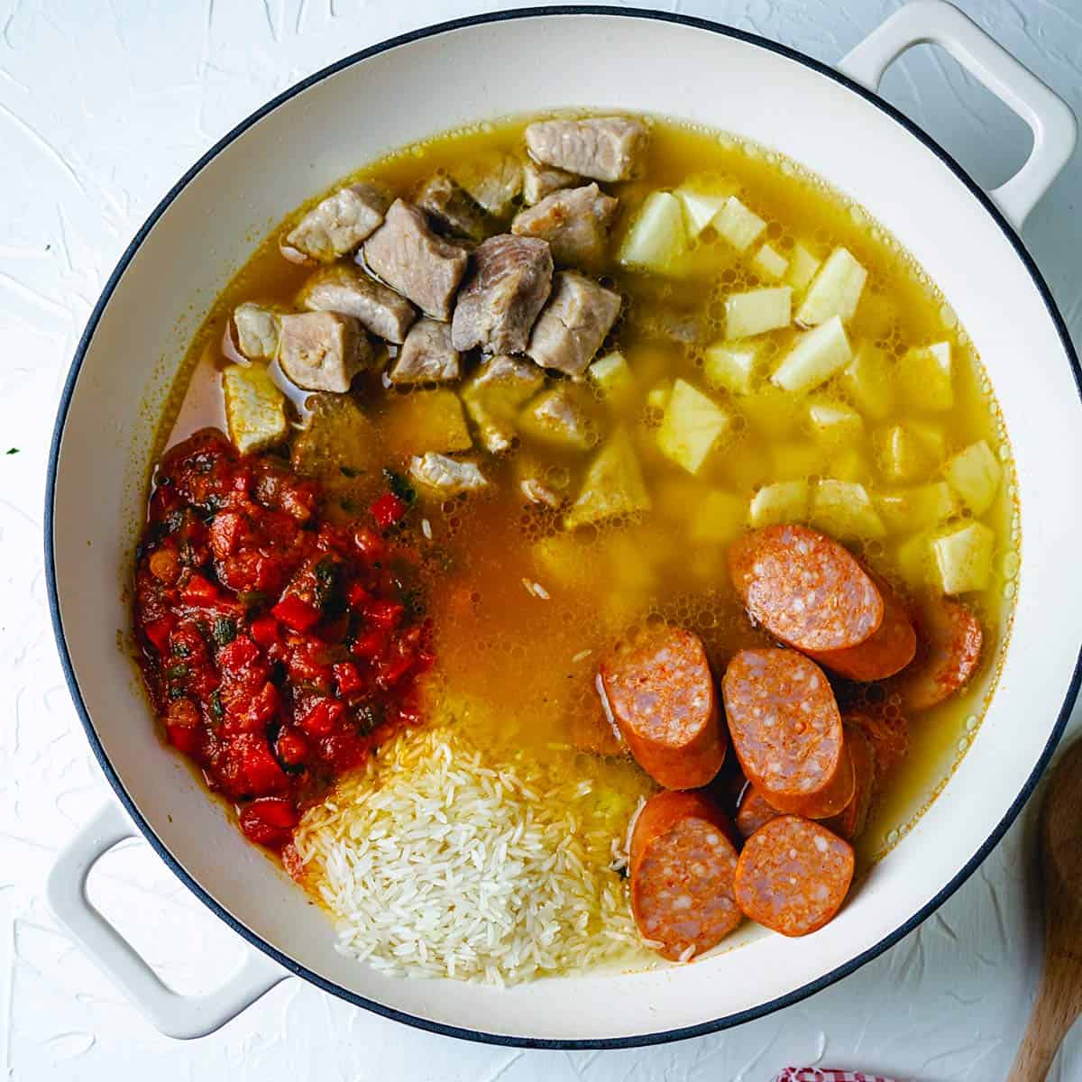 POrk, sausage, potatoes, hogao sauce, rice and broth in a shallow pot. 