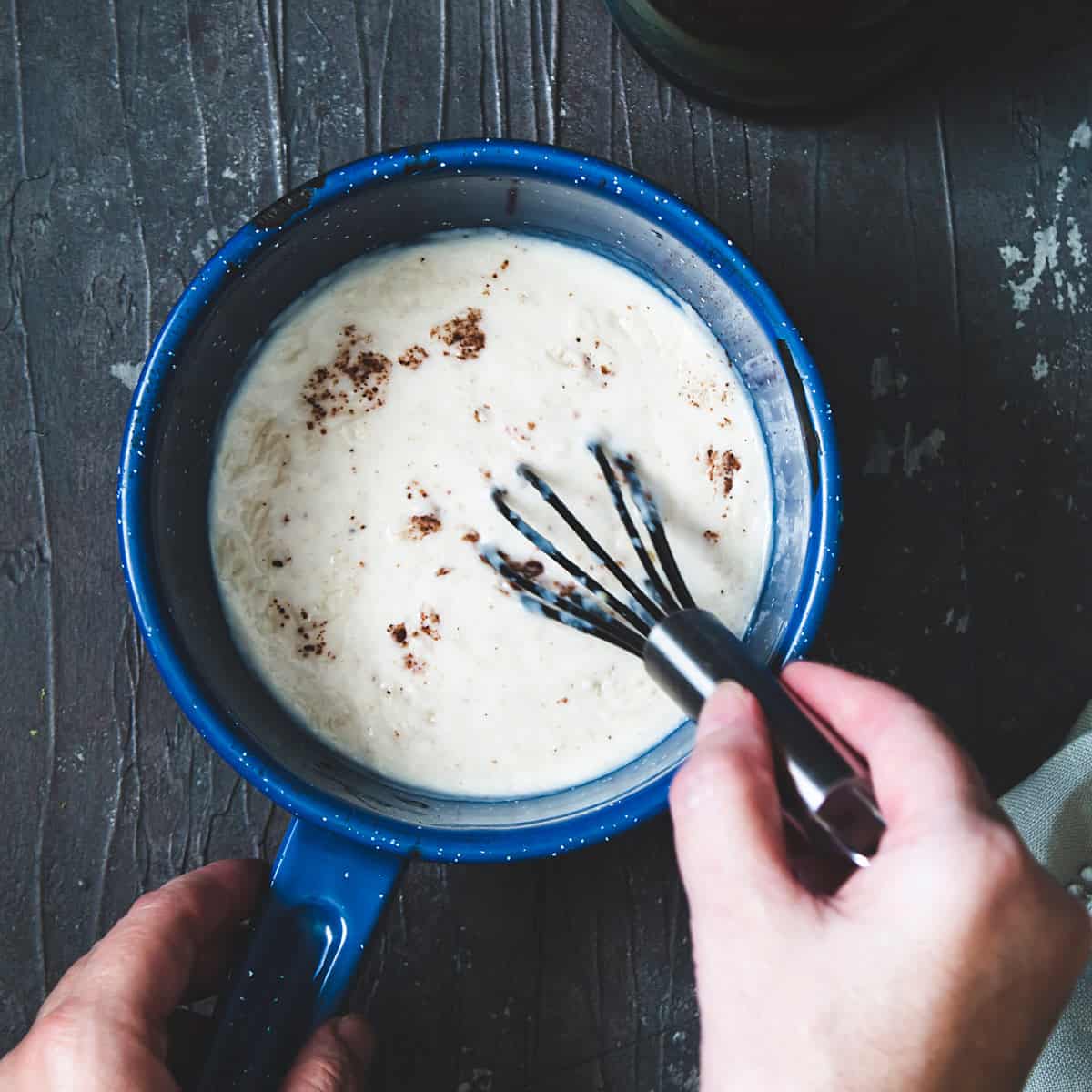 Finished béchamel sauce in a saucepan with a whisk.