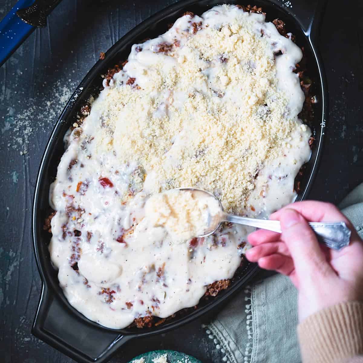 Sprinkling Parmesan cheese over béchamel layer. 