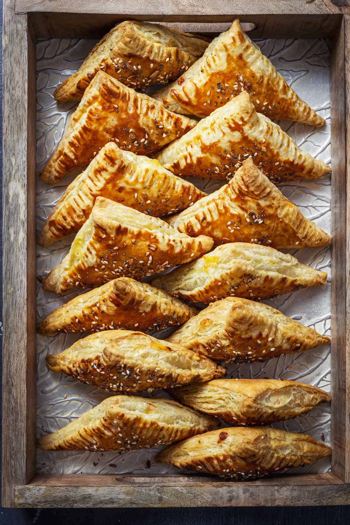 Baked borekas triangles lined up in a wooden tray.