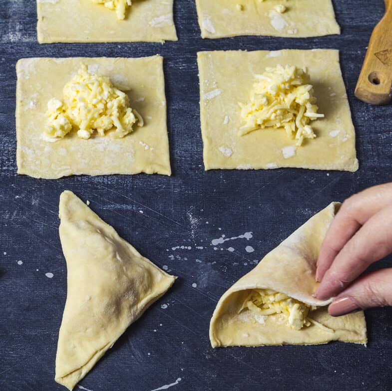 Puff pastry squares with cheese filling on top and some folded into triangles.