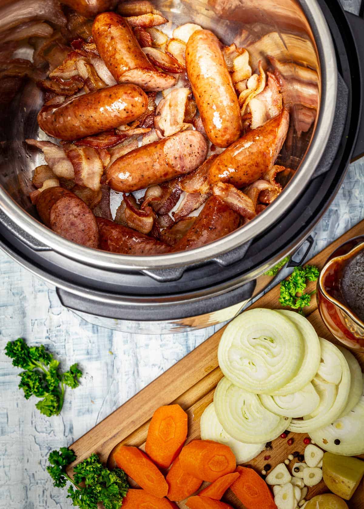 Crispy bacon and sausage in an Instant Pot next to prepared vegetables. 