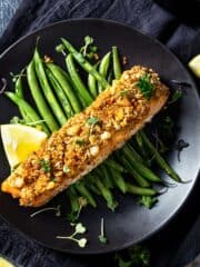 Salmon portion with parmesan and mayo crust over bed of green beans with lemon.