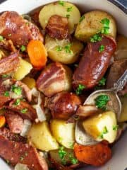 A close up of the potato stew with sausage and bacon in a pot with a spoon.