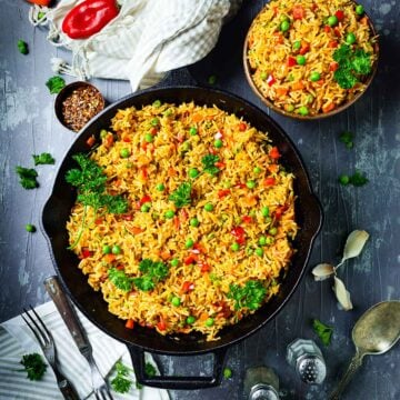 Mixed vegetable rice djuvec in a cast-iron skillet and a bowl on the table.