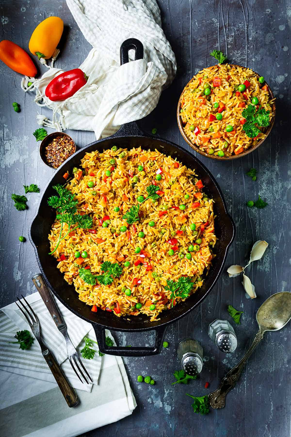 Mixed vegetable rice djuvec in a cast-iron skillet and a bowl on the table.