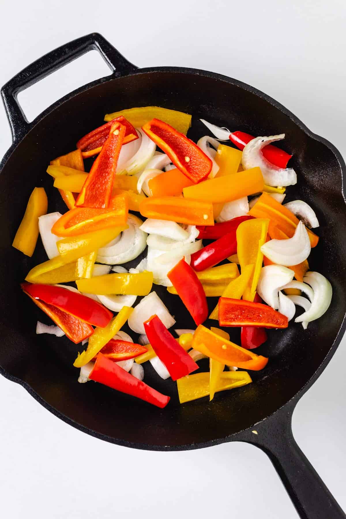 Sliced bell peppers and onions in a cast-iron skillet.