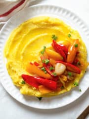 Creamy polenta on a plate topped with sautéed peppers and onions.