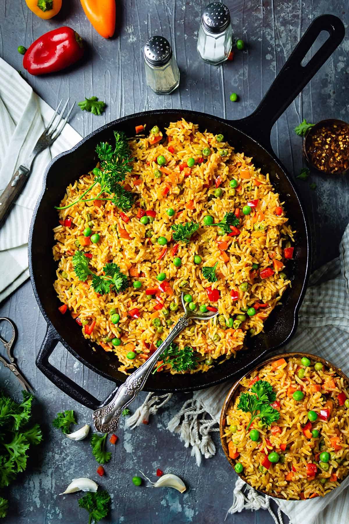 Djuvec rice with mixed vegetables in a skillet and a bowl sprinkled with parsley.