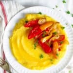 Boiled cornmeal porridge on a plate with roasted peppers and onions.