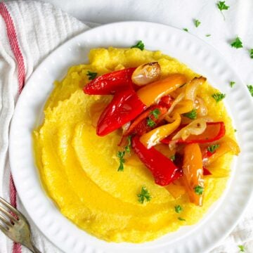 Boiled cornmeal porridge on a plate with roasted peppers and onions.