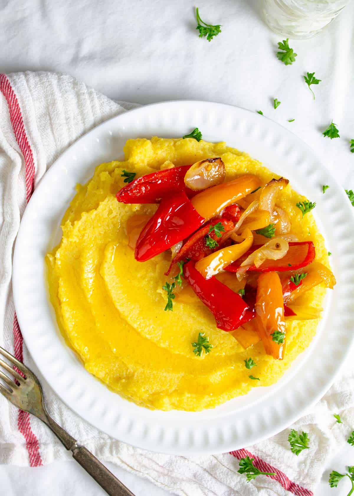 Boiled cornmeal porridge on a plate with roasted peppers and onions.