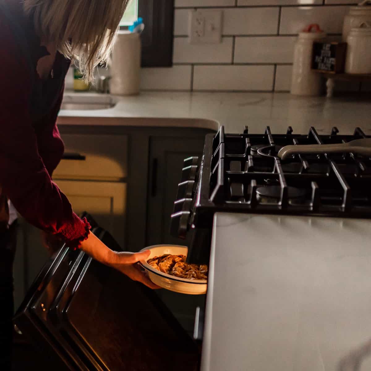 A woman taking phyllo pastry dish out of the oven.