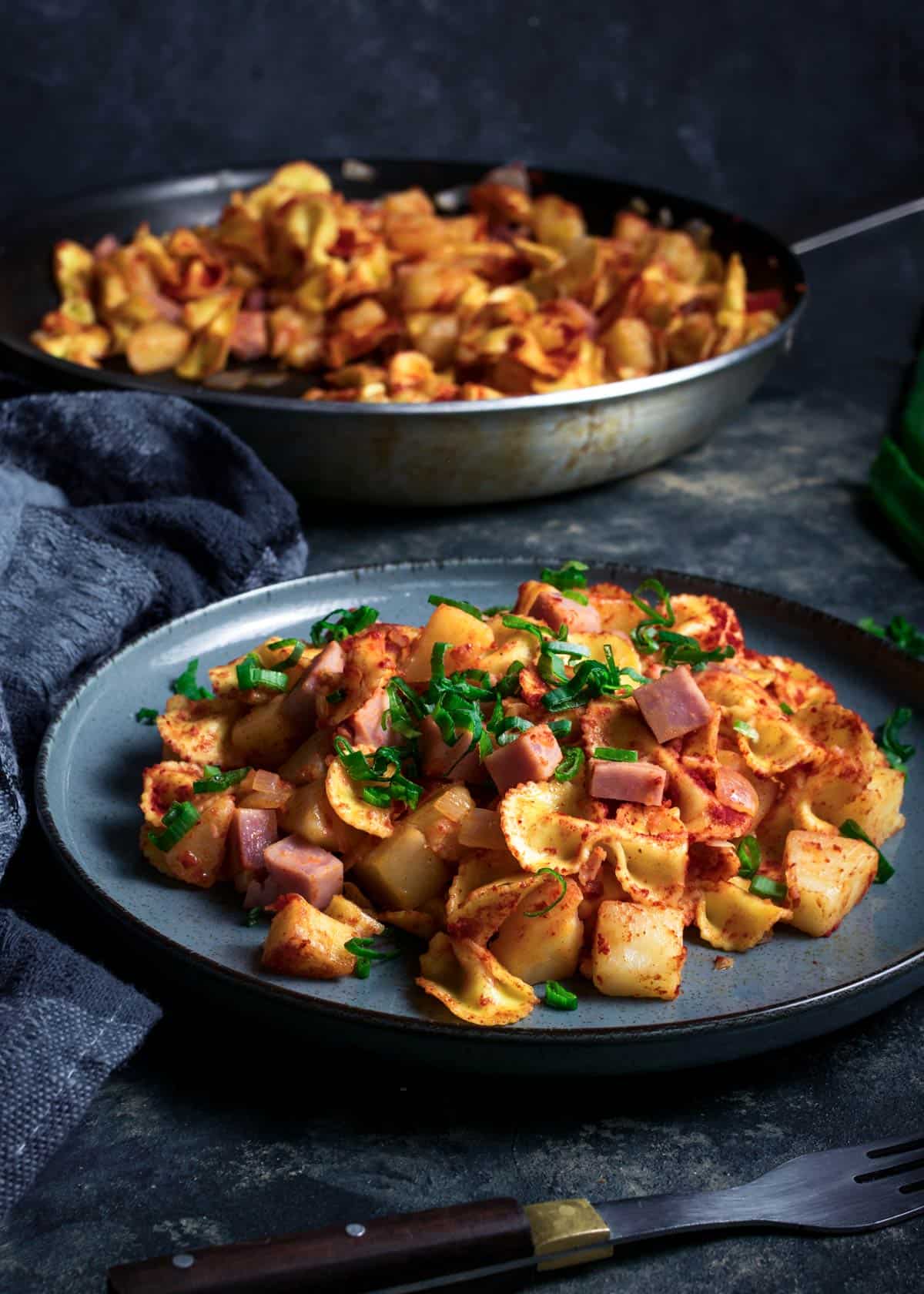 A served plate of potato pasta with ham with a skillet in the background. 