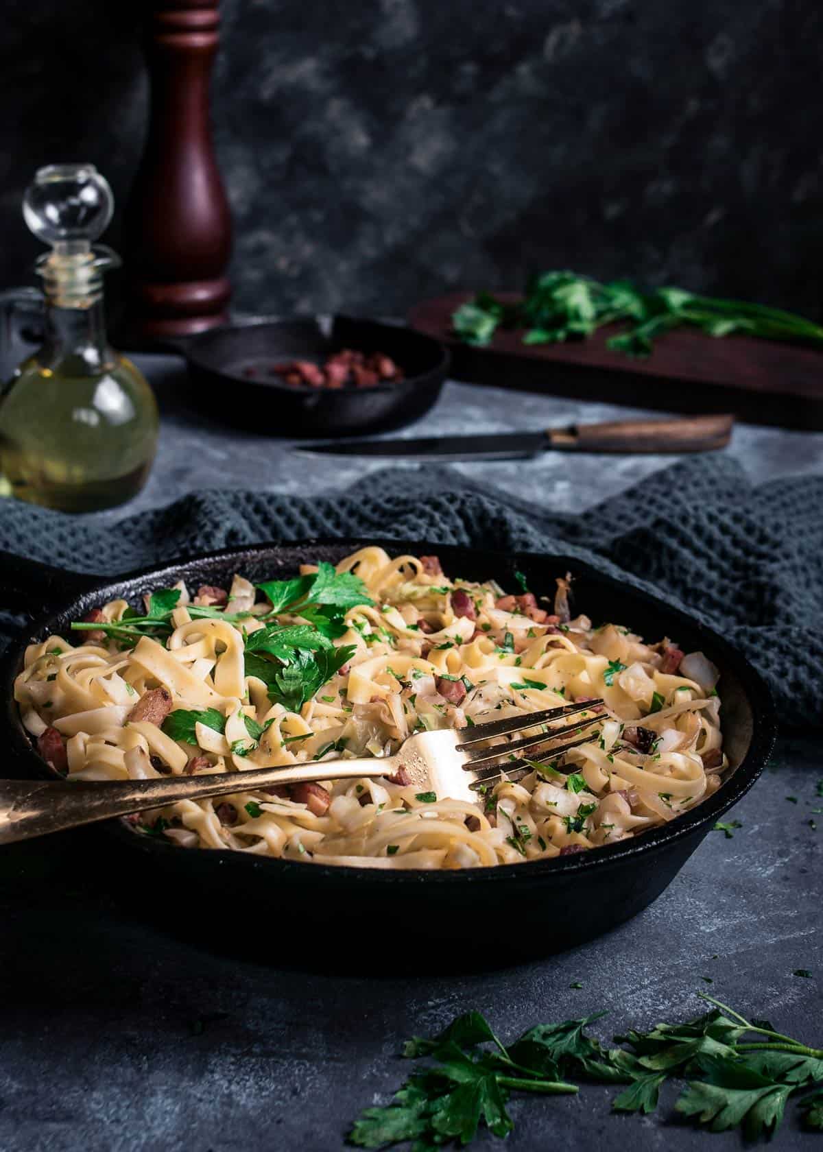 A skillet with haluski sprinkled with fresh parsley on a table with fork.