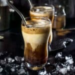 Two glasses with Greek frappe iced coffee with straws and ice with a black background.