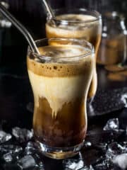 Two glasses with Greek frappe iced coffee with straws and ice with a black background.