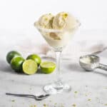 A close up of margarita ice cream scoops in a glass with limes around it.