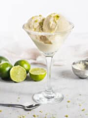 A close up of margarita ice cream scoops in a glass with limes around it.