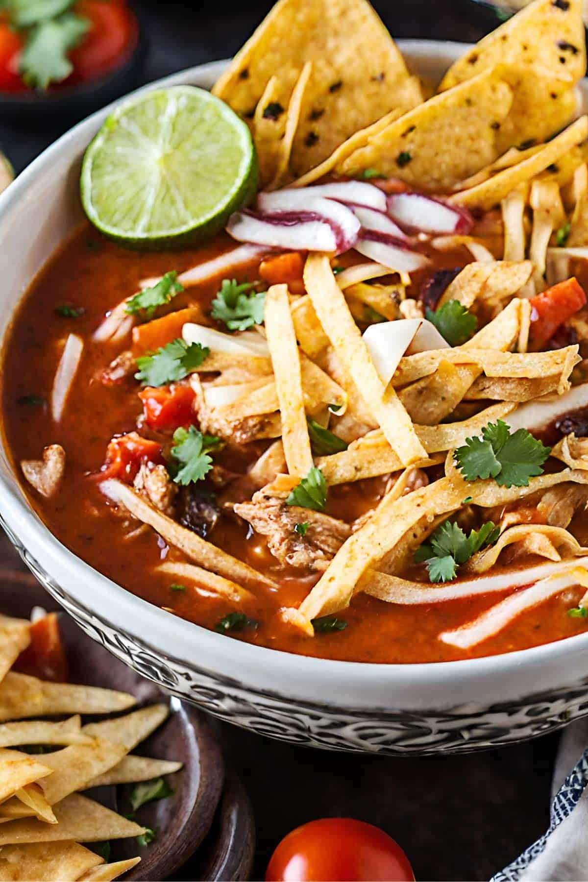 Chicken tortilla soup in a bowl with lime, cilantro and tortilla strips.